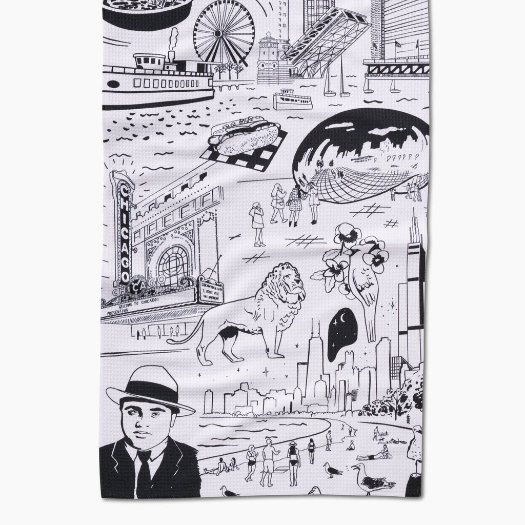 A white tea towel printed with Chicago iconography including the Bean, the Chicago Theater, the Art Institute lions, Lake Michican, and more.