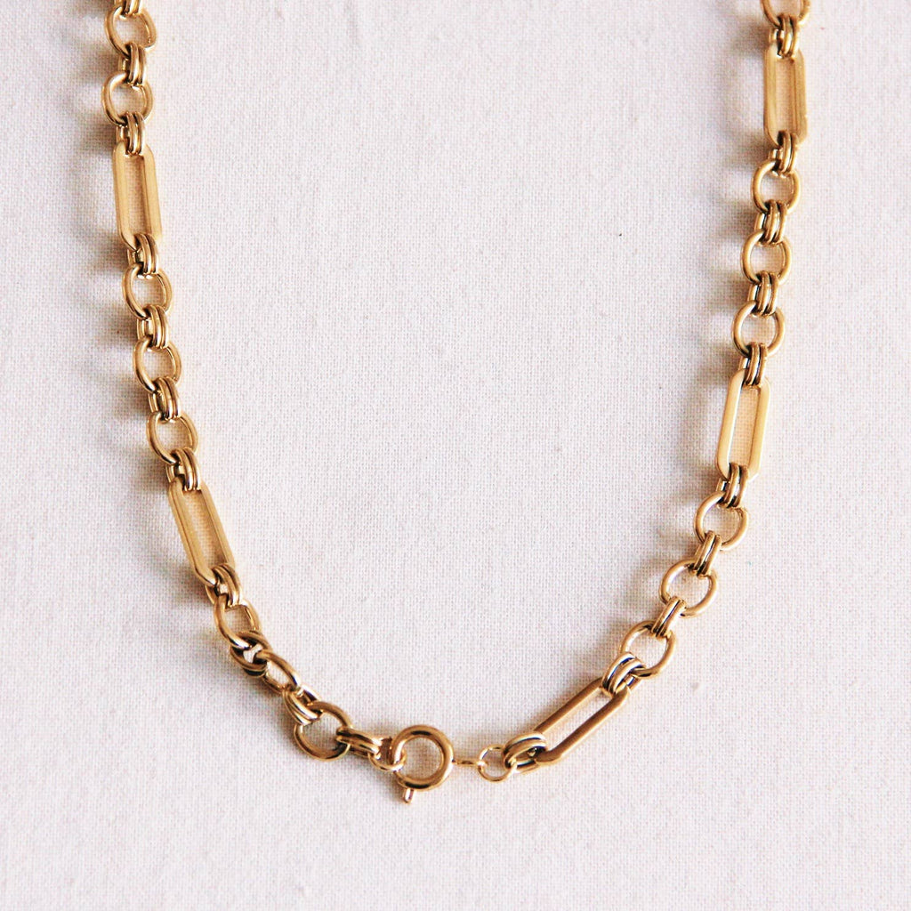 A gold stainless steel chain necklace with a mix of circular links and wide oval links.