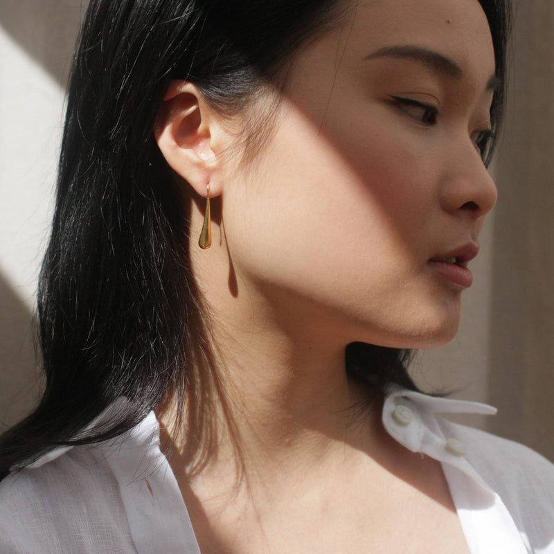 A person wearing the Luxe Gold Droplet Earrings with a ray of sun hitting the ear.