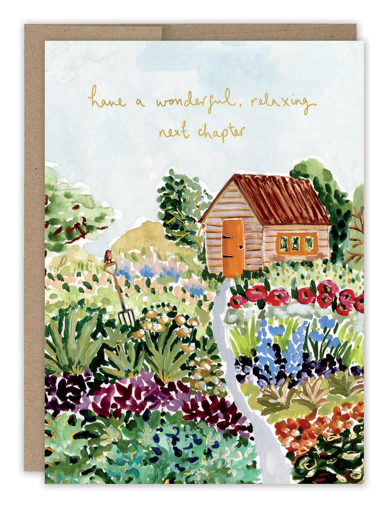 A retirement card gouache illustrated with a log cabin surrounded by flowers and trees below the words "Have a wonderful, relaxing next chapter" in gold foil.