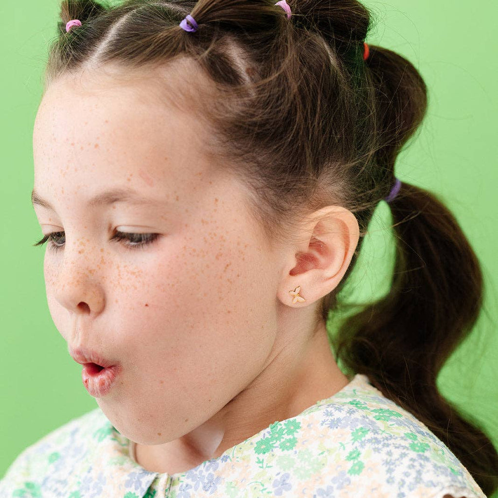 A young girl wearing the Blush Butterfly earrings while blowing out candles out of frame.