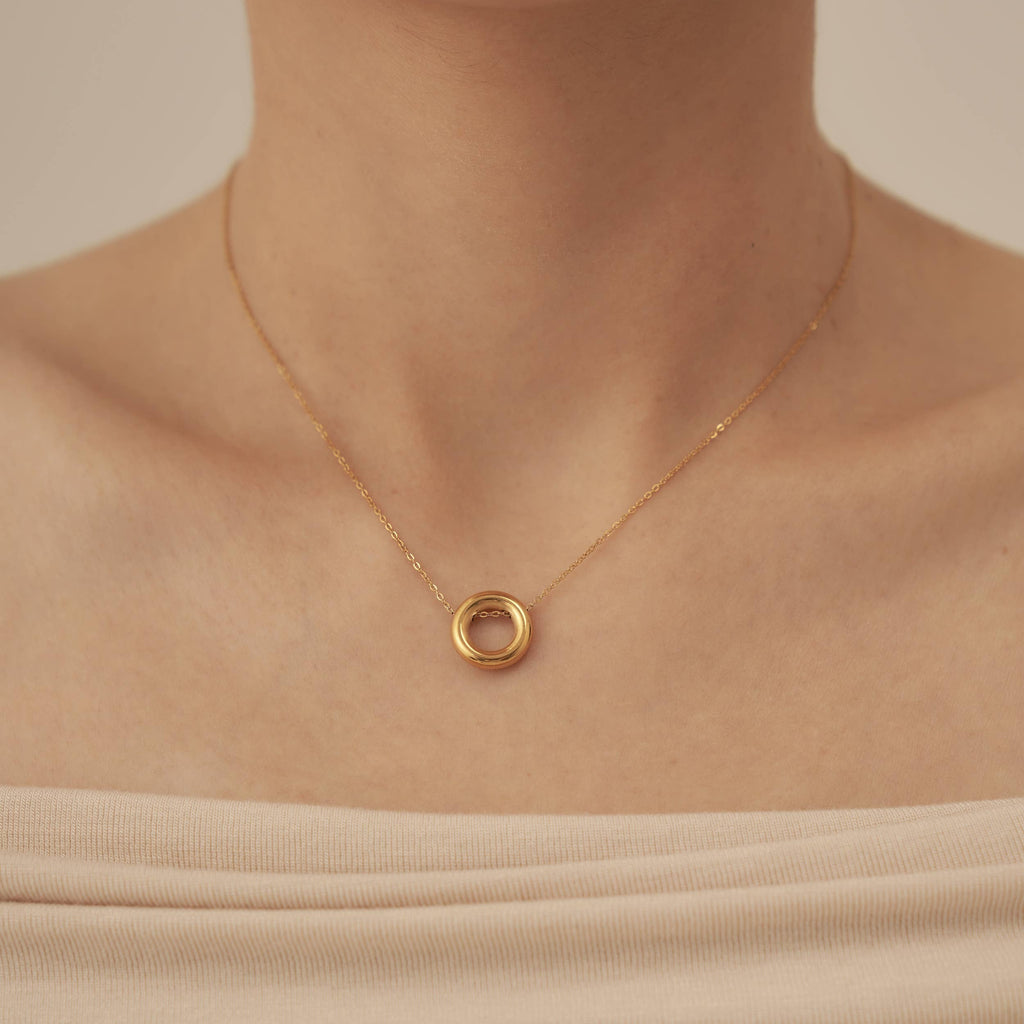 A person wearing a fine chain necklace with a gold plated stainless steel hollow hoop pendant.