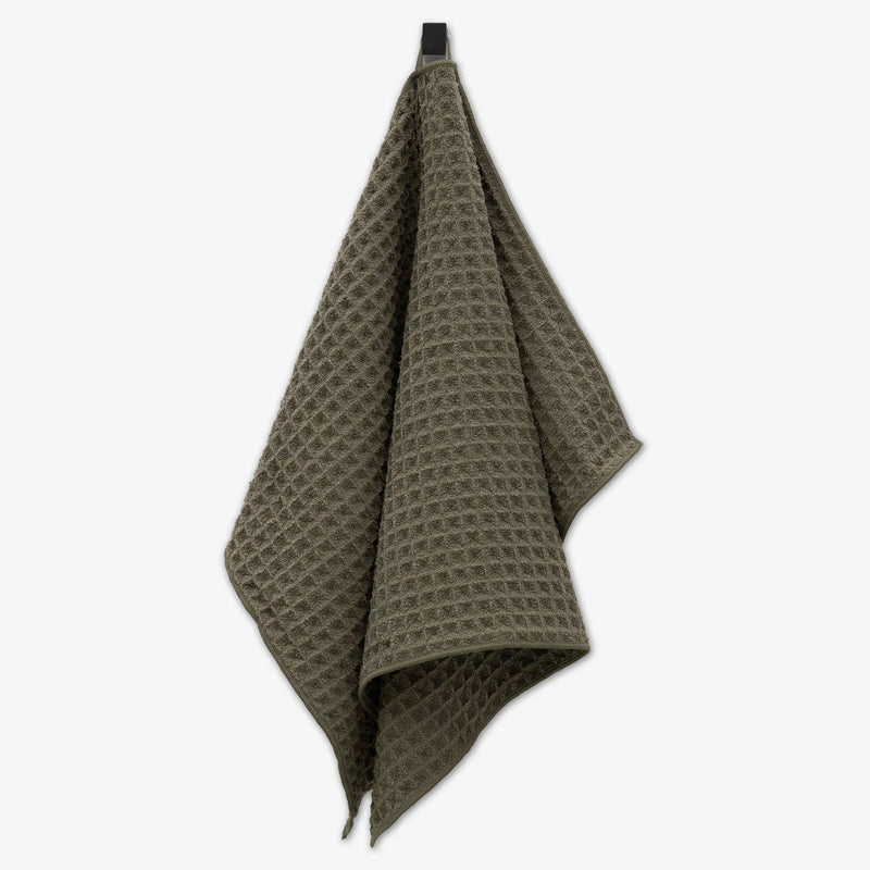 An olive green waffle texture hand towel hanging from an attached fabric loop.