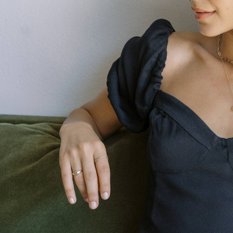 A person wearing the Flora Signet Ring in Gold while lounging on a couch.