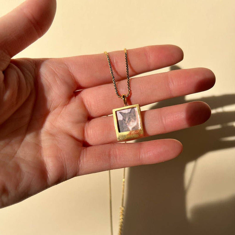 A person holding the Polaroid Photo Charm on a necklace chain.