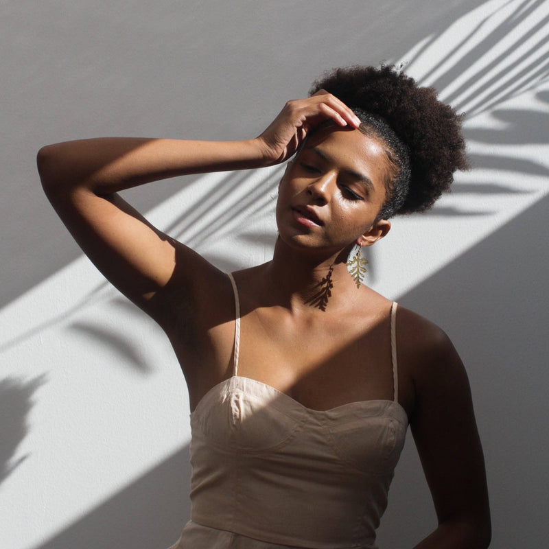 A person wearing the Fern Leaf Earrings  with its shadow cast across their neck.