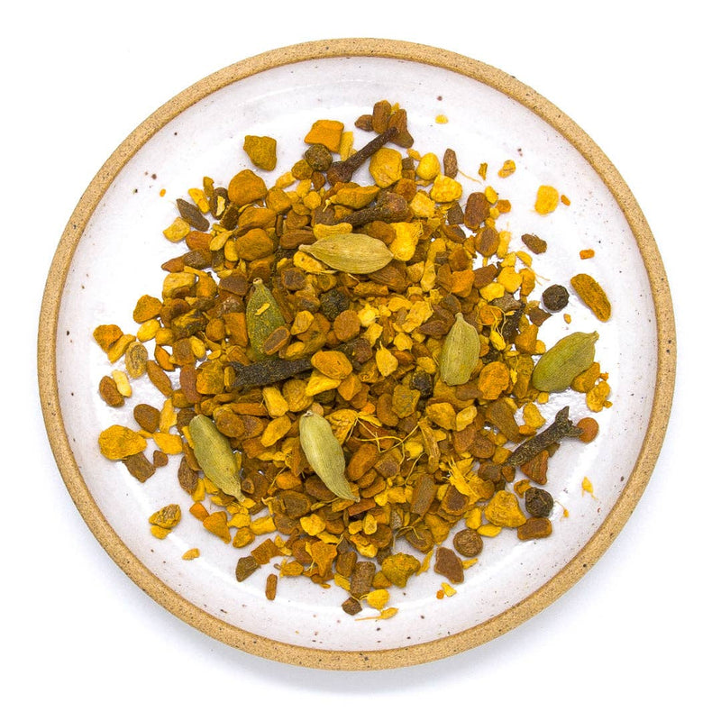 A ceramic plate filled with turmeric, ginger, cinnamon, cardamom, clove and black pepper.