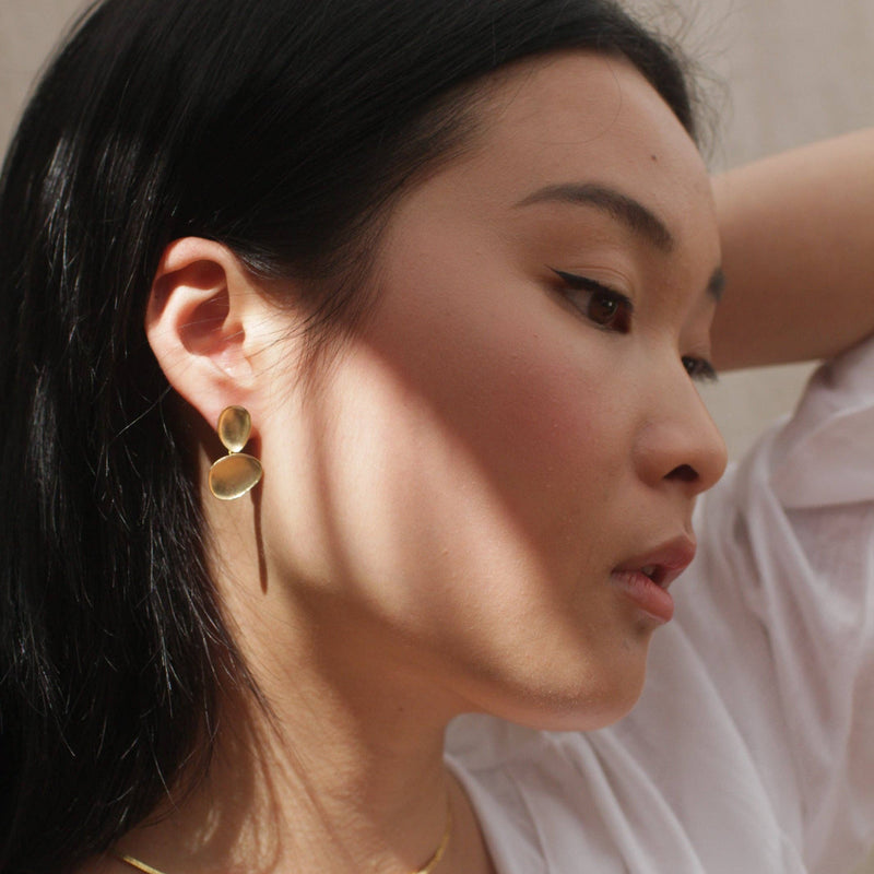 A person wearing the Luxe Gold Baubles Earrings with a ray of sun across the ear.