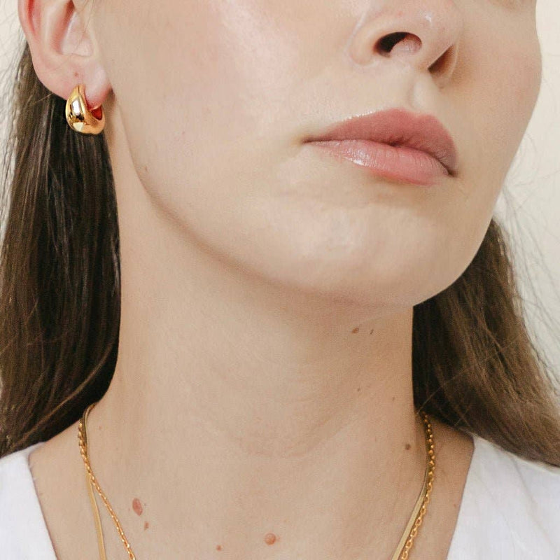 A person looking to their left while wearing the Dumpling Hoops in Gold.