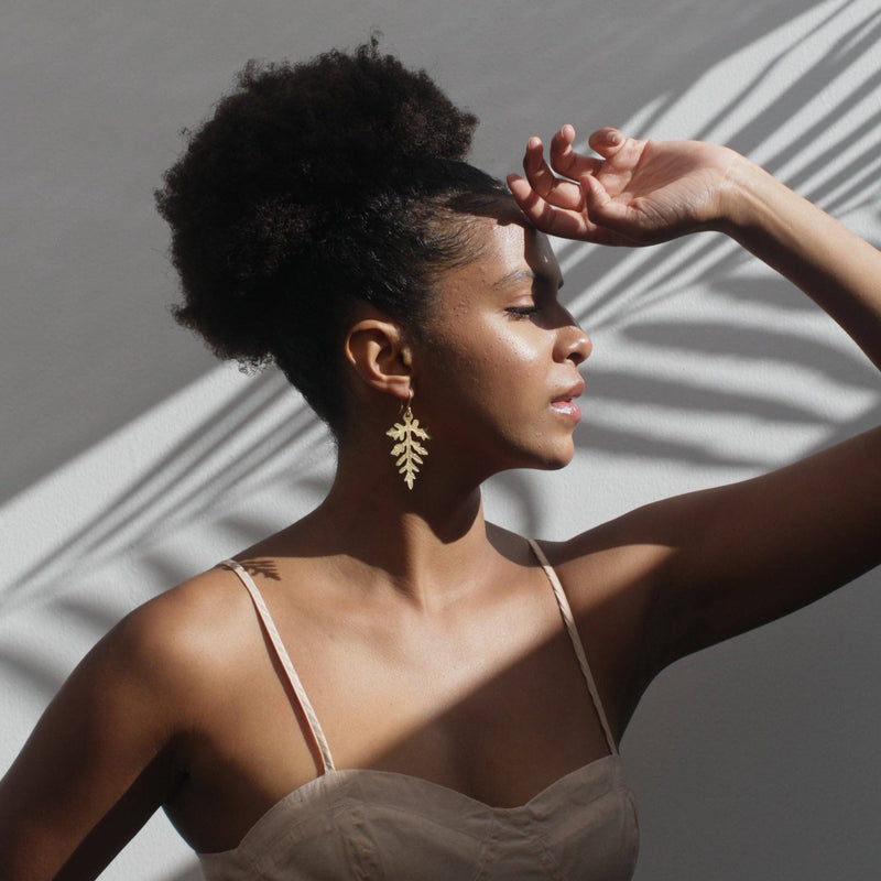 A person wearing the Fern Leaf Earrings with their hand up against the sun.