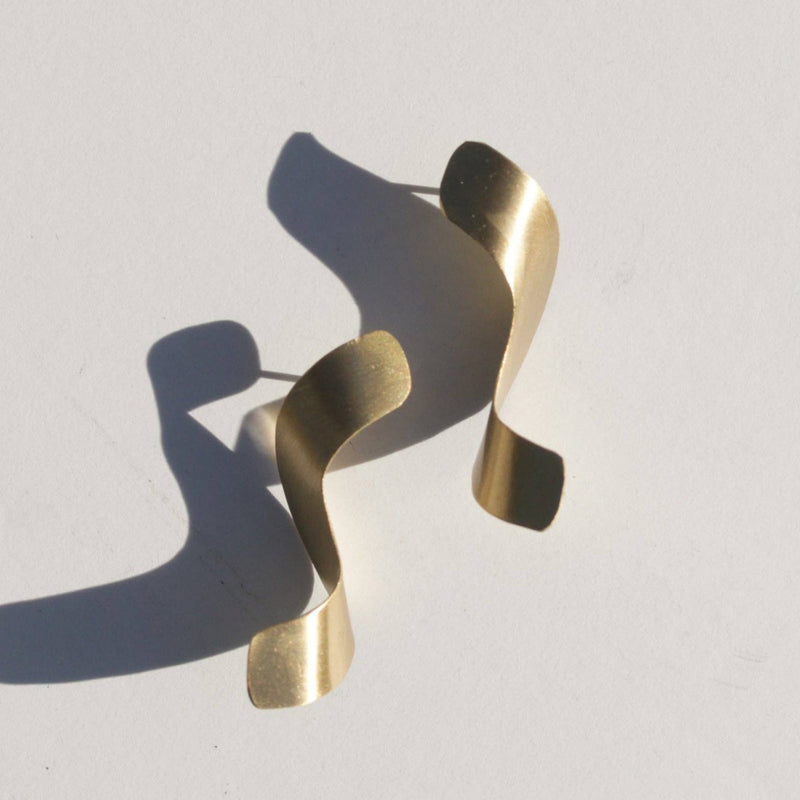 Two stud earrings with a curved plate of brass in an abstract noodle shape.