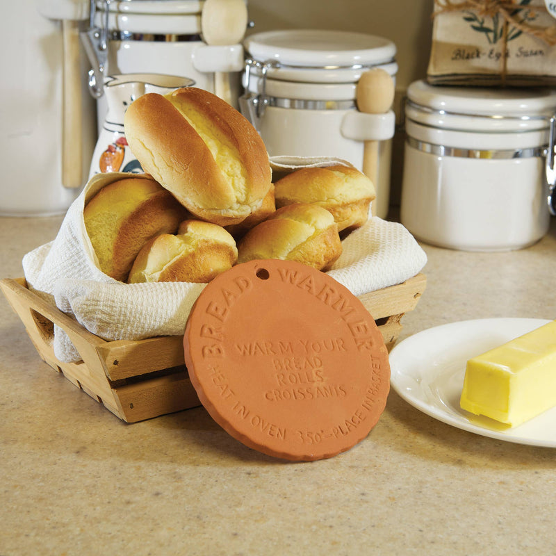 A terracotta bread warmer against a pile of bread loaves.