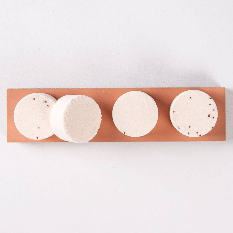 Four pink grapefruit shower steamer discs sitting on a ceramic plank.