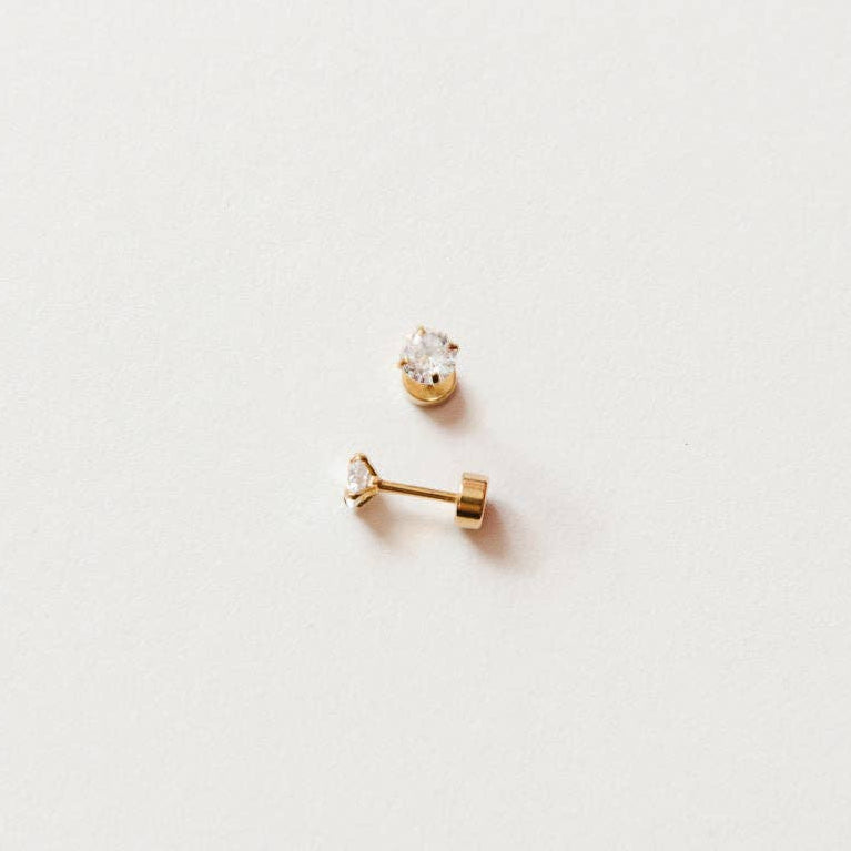 A pair of gold stud earrings with prongs around a single crystal and a flat post backing.