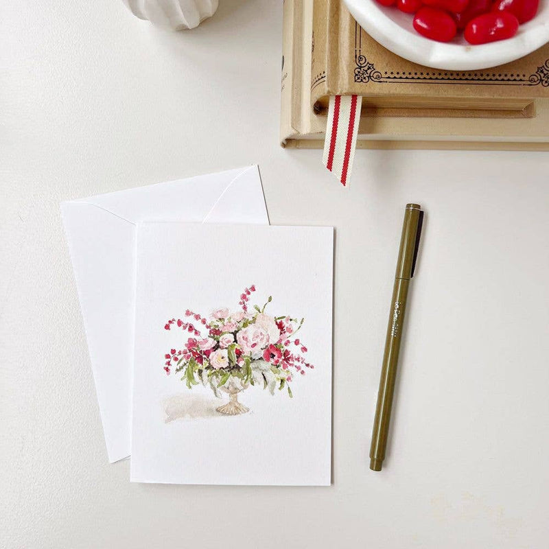 A Pinks Bouquet Notecard on a desk next to a pen, a stack of books, and a bowl of red candies.