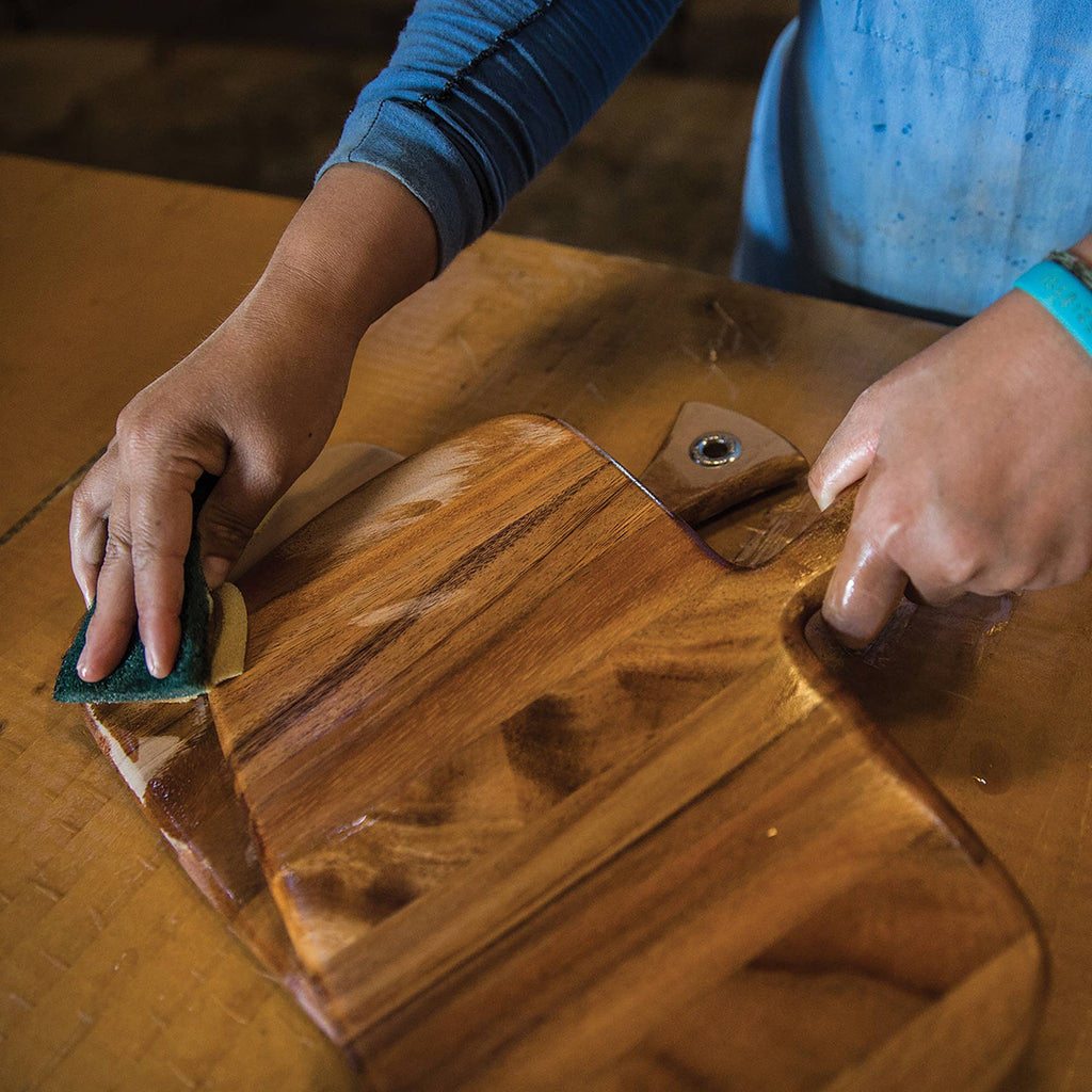 A pair of hands using the Butcher Block Oil to clean a wooden cutting board.