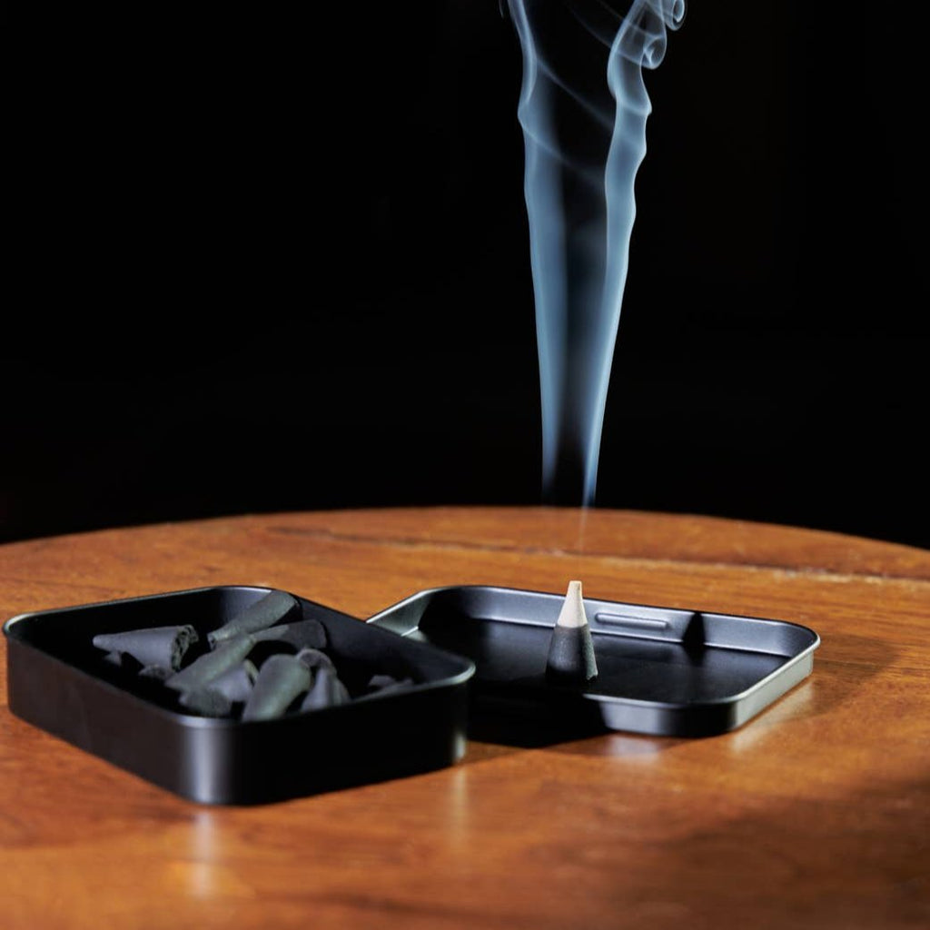 A burning incense cone on the lid of its container.