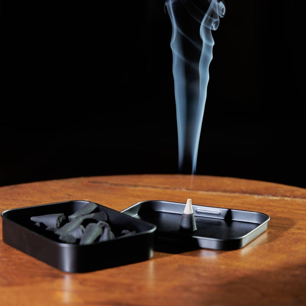 An incense cone burning on the lid of its container.