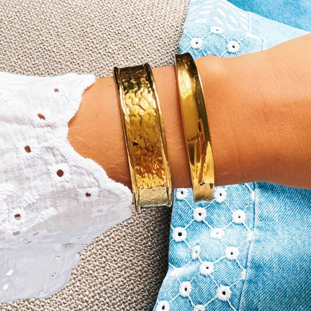 A wrist wearing the Wide Hammered Bracelet in Gold next to the Flared Bangle in Gold.