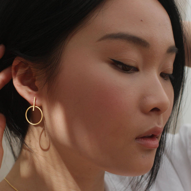 A person wearing the luxe Gold Outline Earrings in the sun.