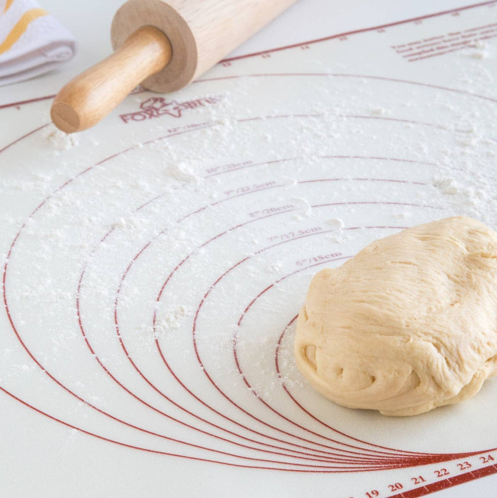 A rolling pin and dough on a flour-covered baking mat.