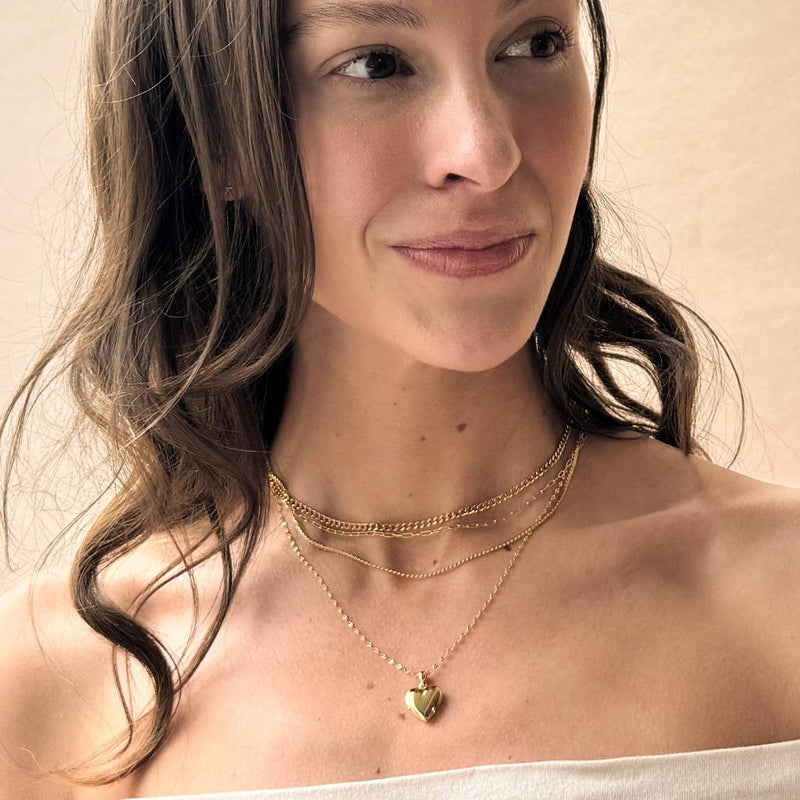 A person wearing the Golden Heart Locket stacked with fine chain necklaces. 