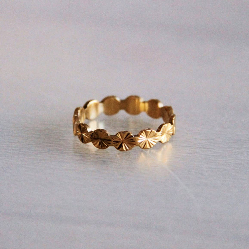 A gold stainless steel ring patterned with tiny circular sun bursts.