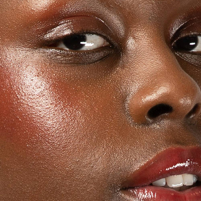 A person with dark tone skin wearing Red-dy or Not Lip & Cheek Tinted Balm on their eyes, cheekbones, and lips.