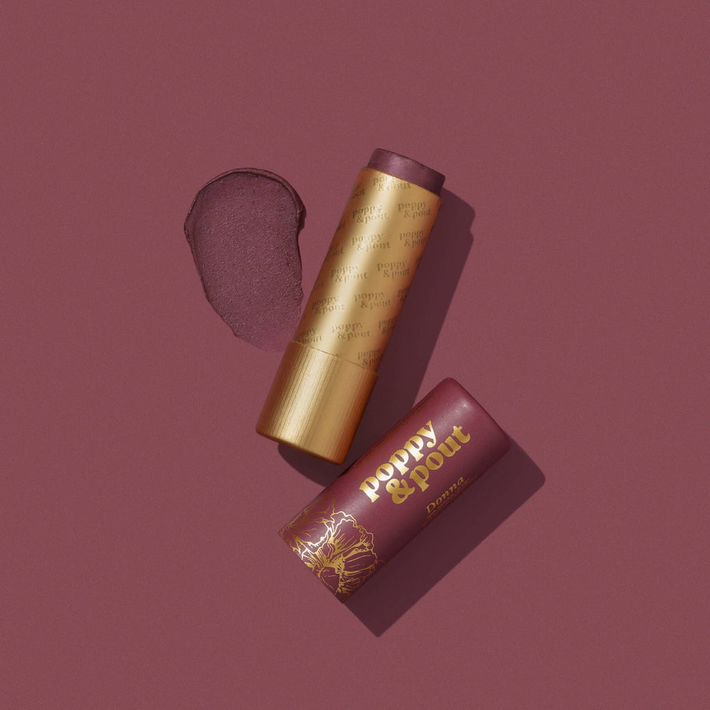 A dark plum Donna Lip Tint with a gold tube next to its lid and a swatch against a similarly colored background.