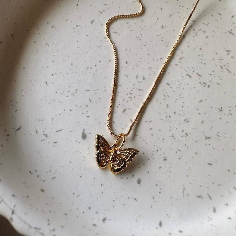 The Butterfly Necklace in Gold resting on a white speckled ceramic plate.