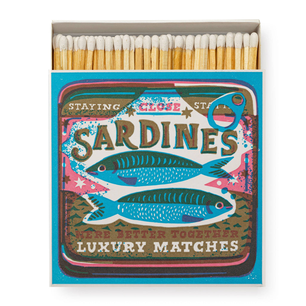 A square matchbox illustrated with a screenprinted sardines can with the words "Staying Close Staying Here Better Together" and filled with white tipped matches.