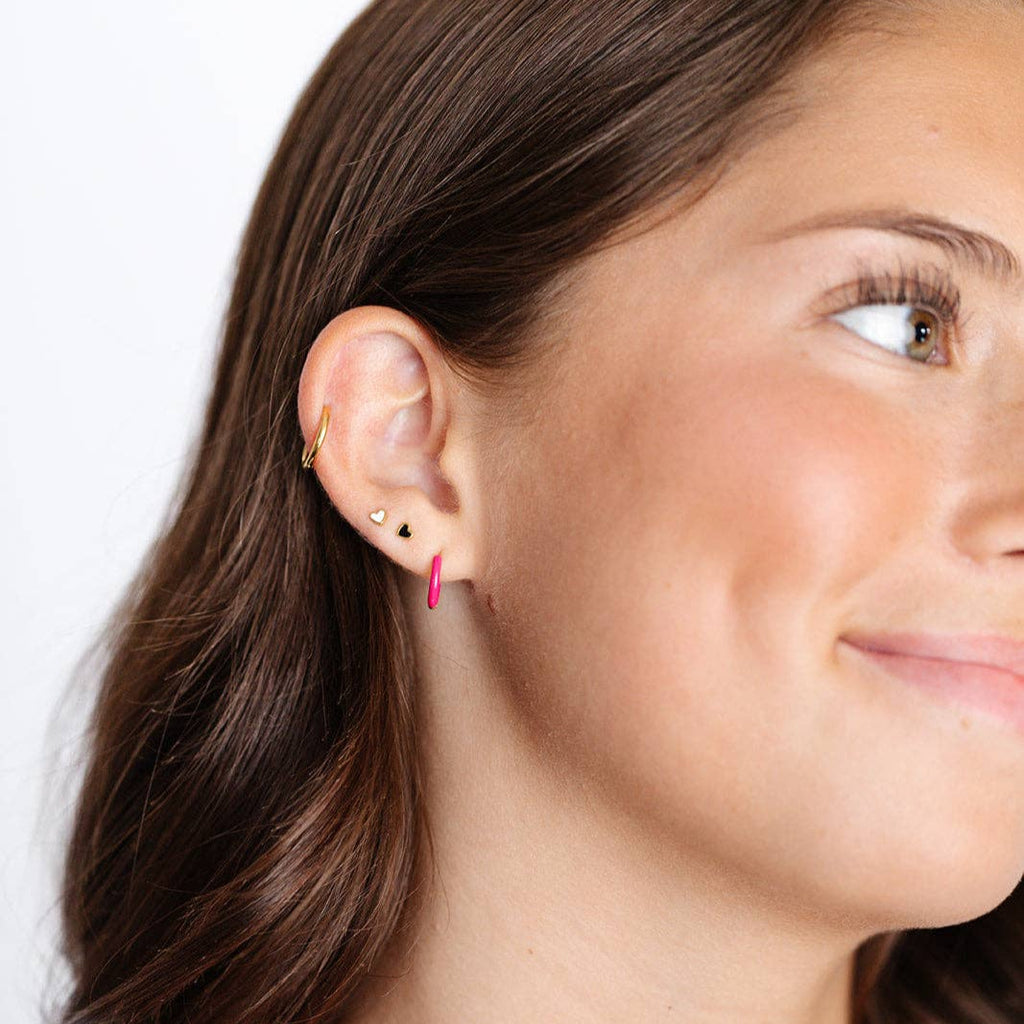 A person wearing the mini Enamel Heart Stud Earrings in Black and White along their earlobe.