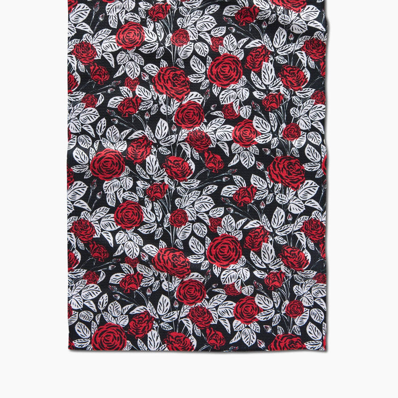 A black tea towel patterned with red roses and white stems and leaves.