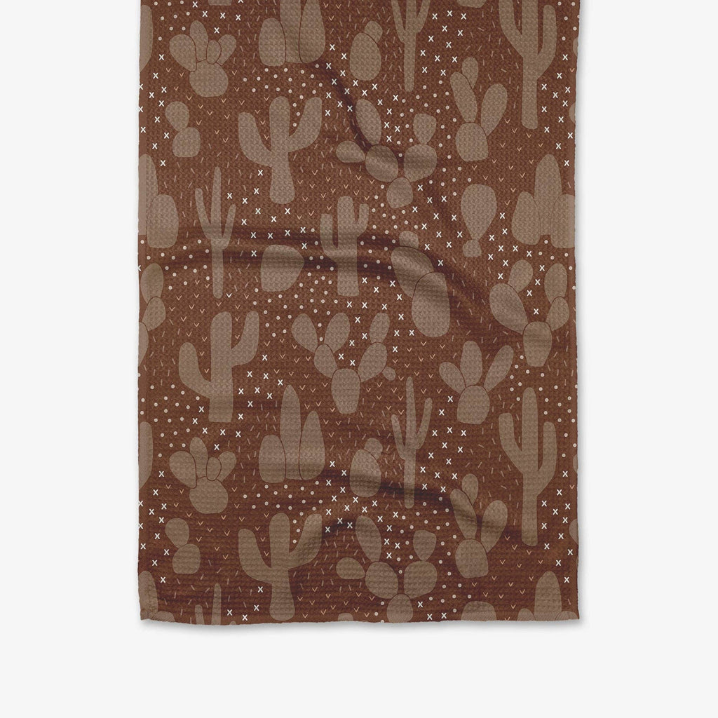  A brown tea towel patterned with light brown cacti and desert flowers.