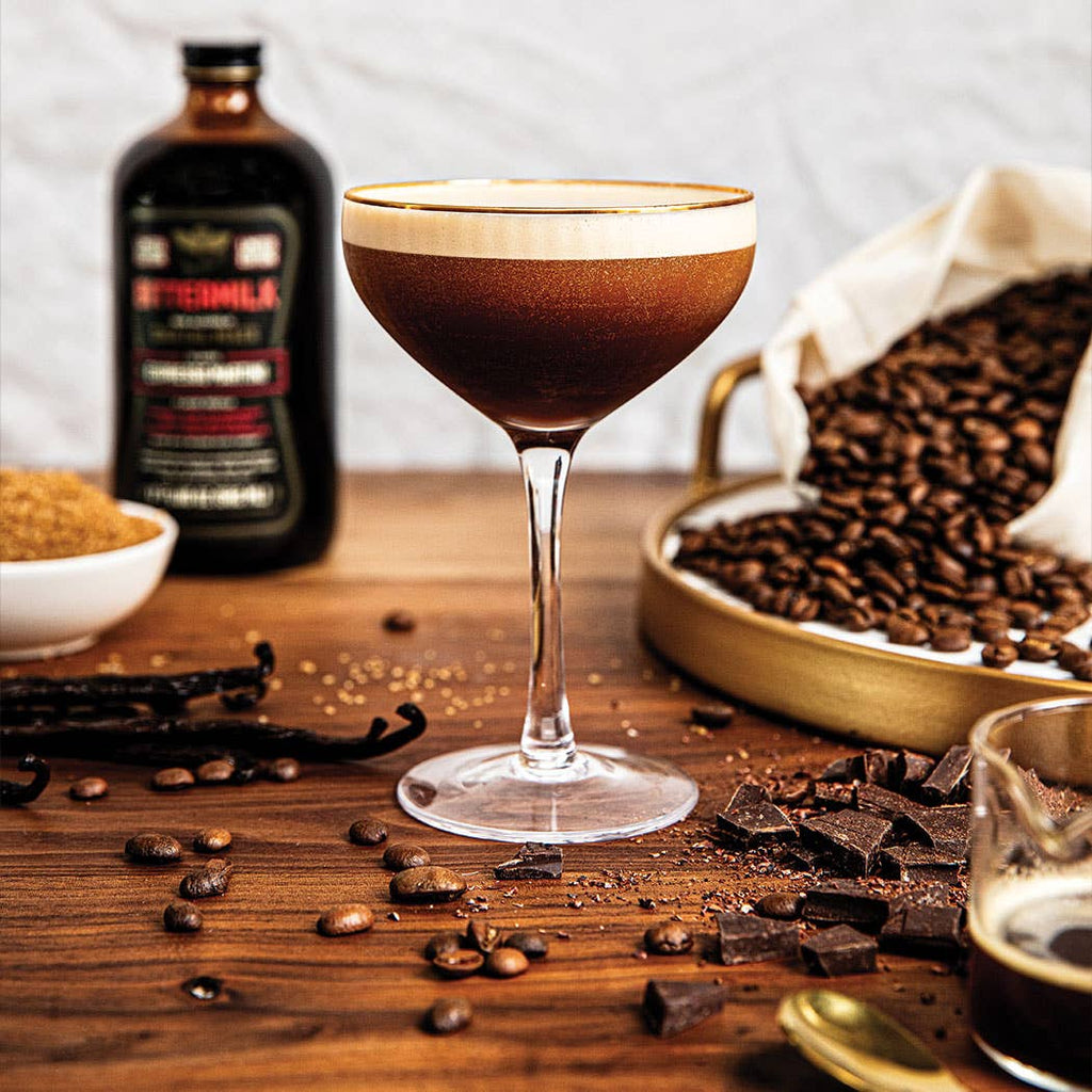 A Bittermilk Espresso Martini surrounded by cocoa bits, espresso beans, brown sugar, and the bottle.