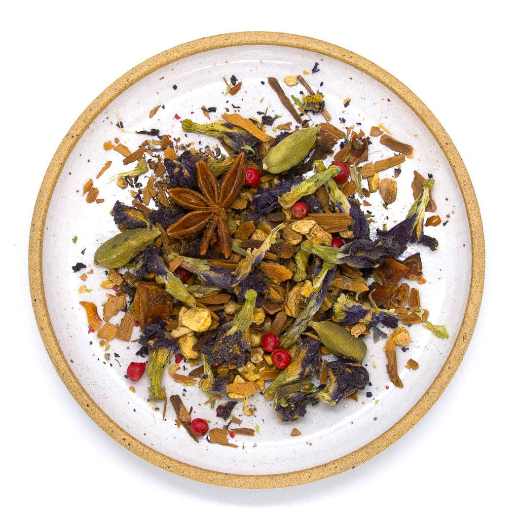 A ceramic plate filled with chai spices, ginger, and dried butterfly pea flowers.