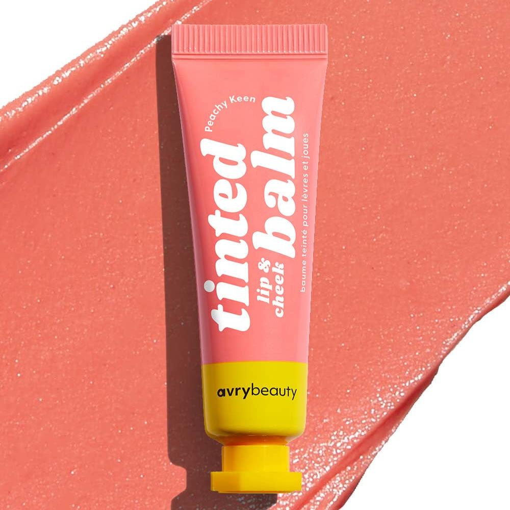 A pink tube of Peachy Keen Lip & Cheek Tinted Balm in front of a swatch of peach tinted balm.