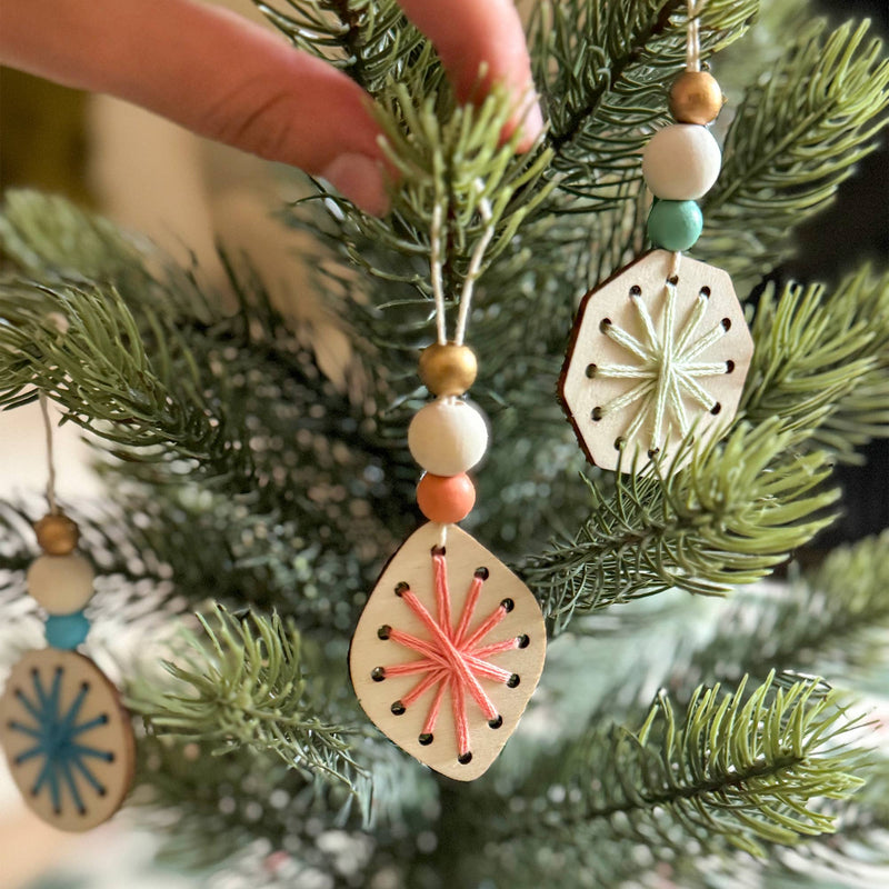 A hand placing a peach threaded snowflake ornament on an evergreen tree.