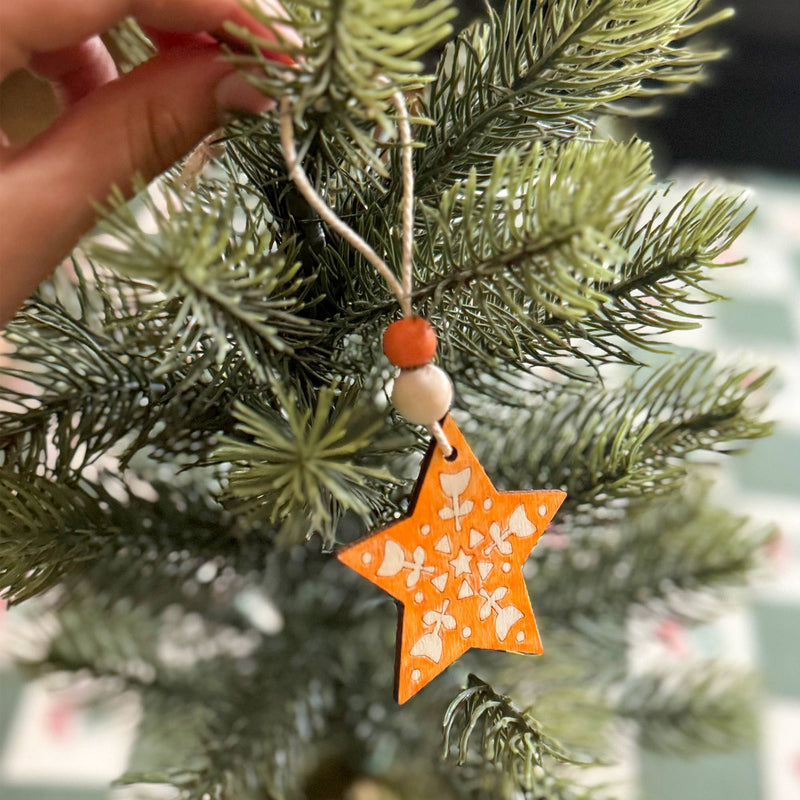 An orange colored wooden star ornament on an evergreen tree.