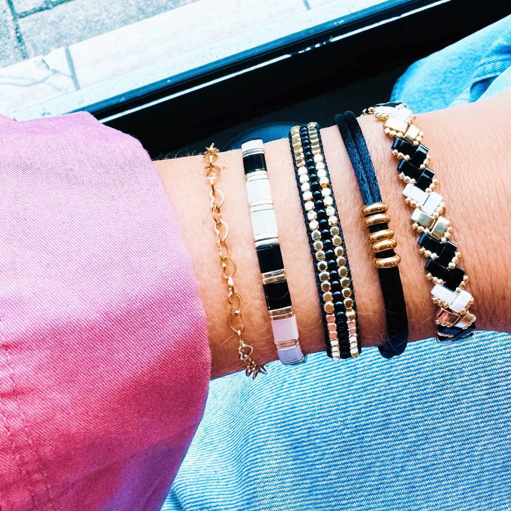 A wrist wearing a stack of black and gold bracelets, including the Black and Gold Woven Bracelet.