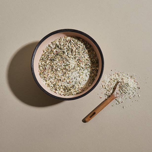 A ceramic bowl of Classic Chip Dip Mix  with a wooden spoon covered in herbs and spices.