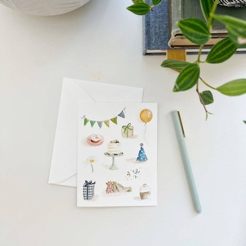 A Celebrate Notecard on a desk next to a pen, a stack of books, and a potted plant.