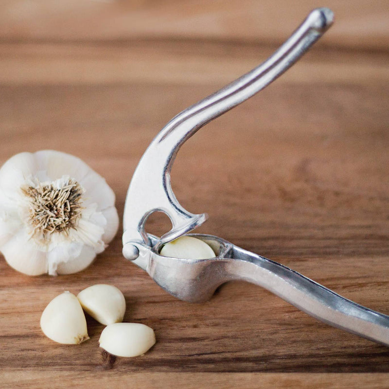 A Garlic Press closing on a garlic clove next to a garlic and a few cloves.