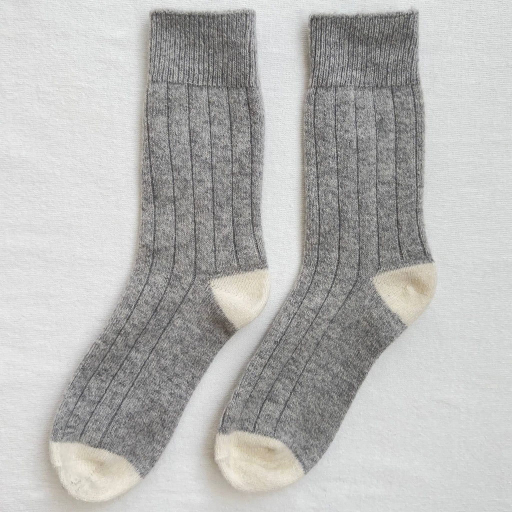 A gray knitted pair of socks with cream color blocking at the heels and toes.