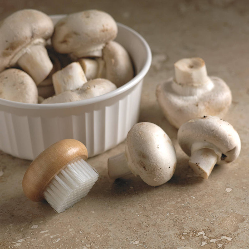 A mushroom brush next to a bowl of small white mushrooms.