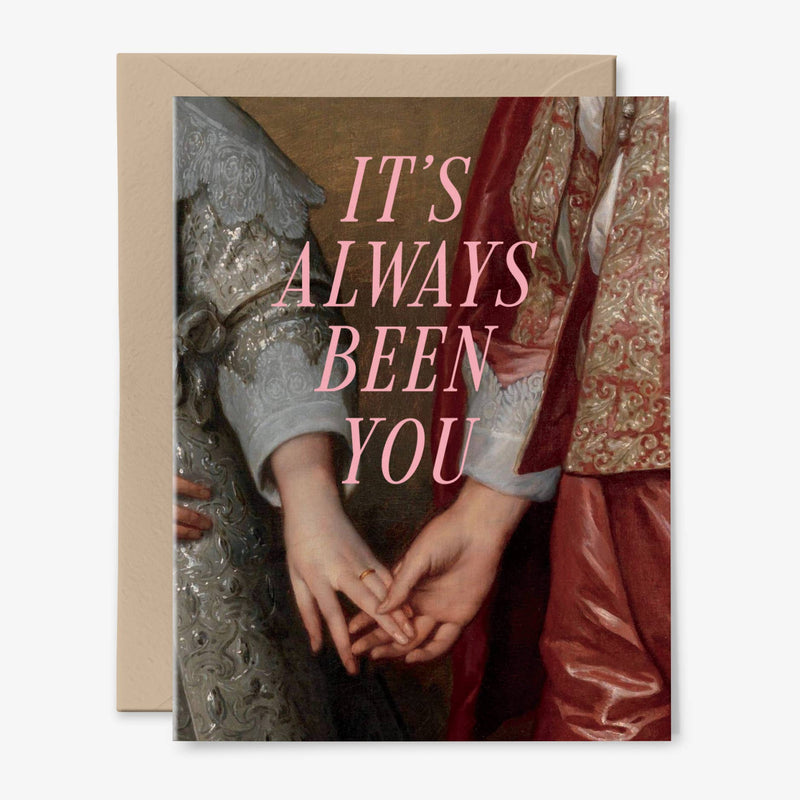 A card illustrated with a 17th century painting of two people holding hands behind the words "It's Always Been You" in pink. There is a kraft envelope behind.