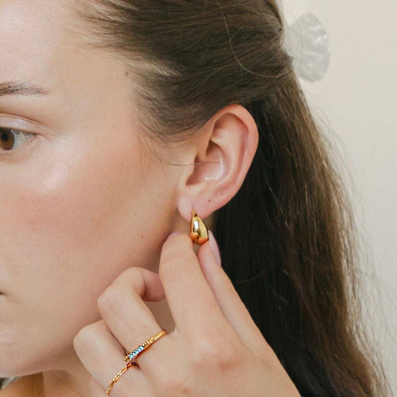 A person pulling out the Dumpling Hoops in Gold from their ear.