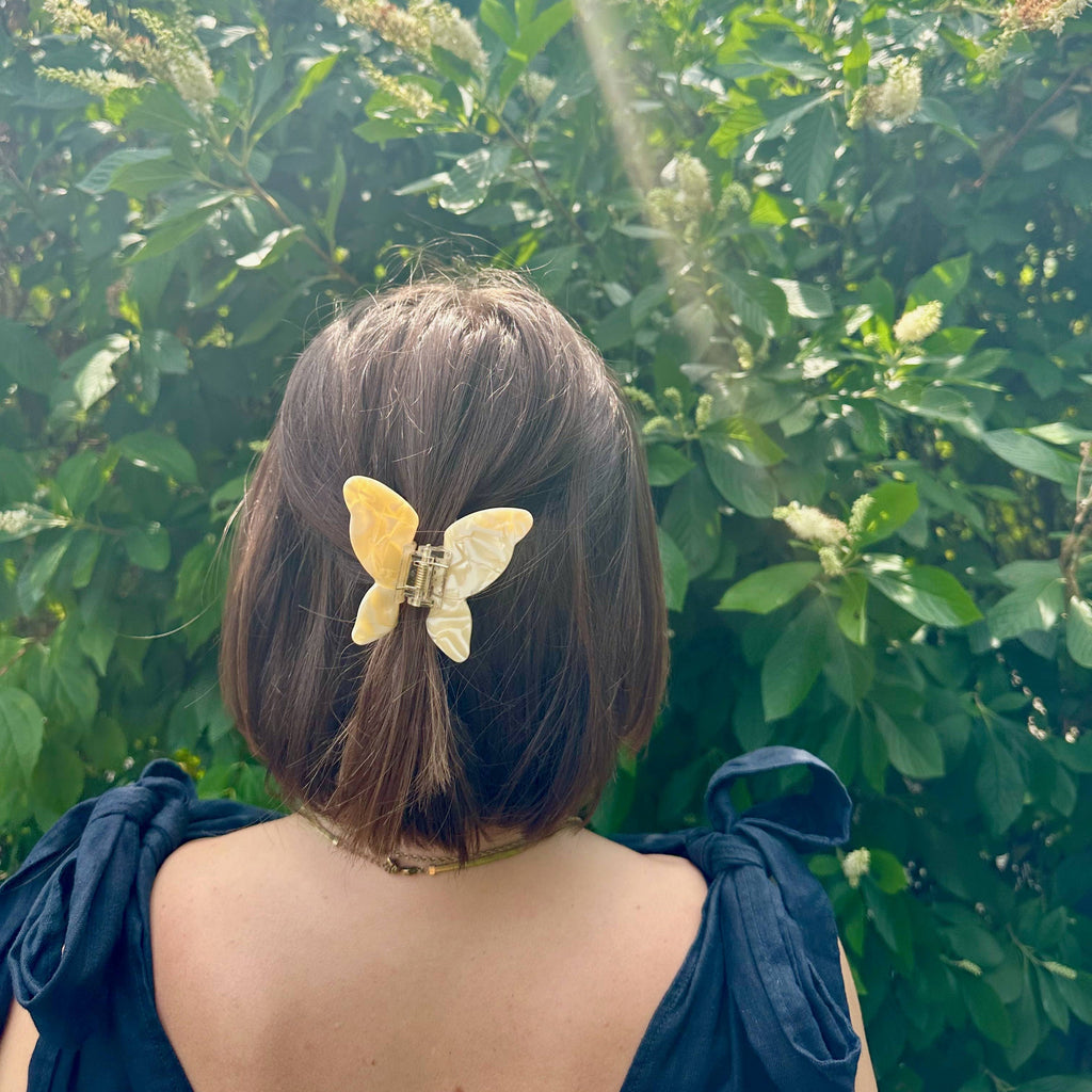 A person wearing their shoulder length hair half up using a yellow butterfly claw clip.