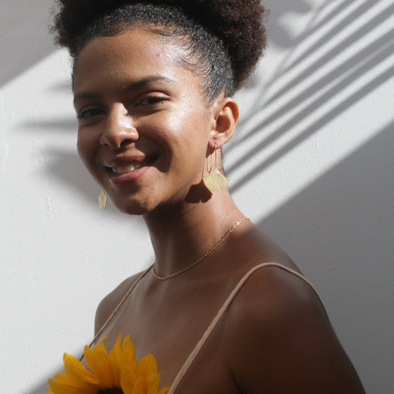 A person smiling at the viewer wearing the Gingko Leaf Earrings.