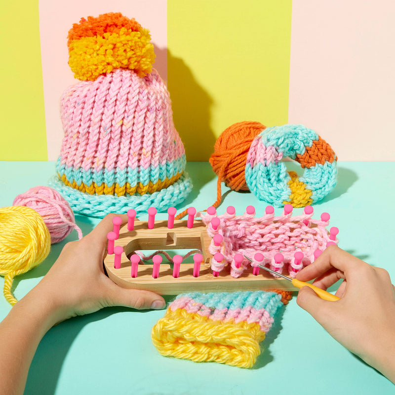 A pair of hands using the loom to knit with pink yarn.